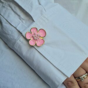 Knapp-smycket Cleo i färgen Rosa, blomformat smycke som sitter på en vit skjortärm.